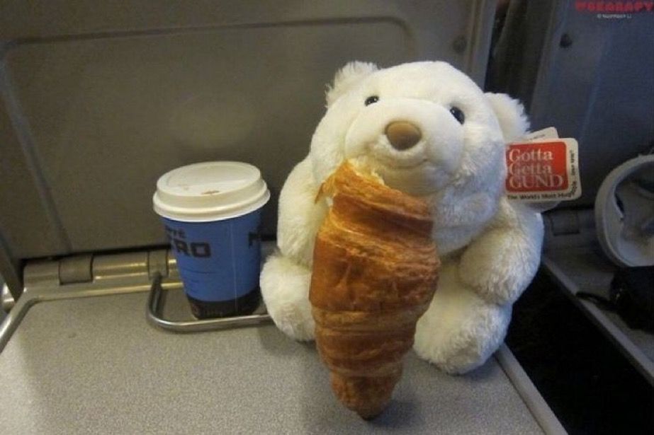 Snuffles the bear enjoying a croissant and coffee on a train.