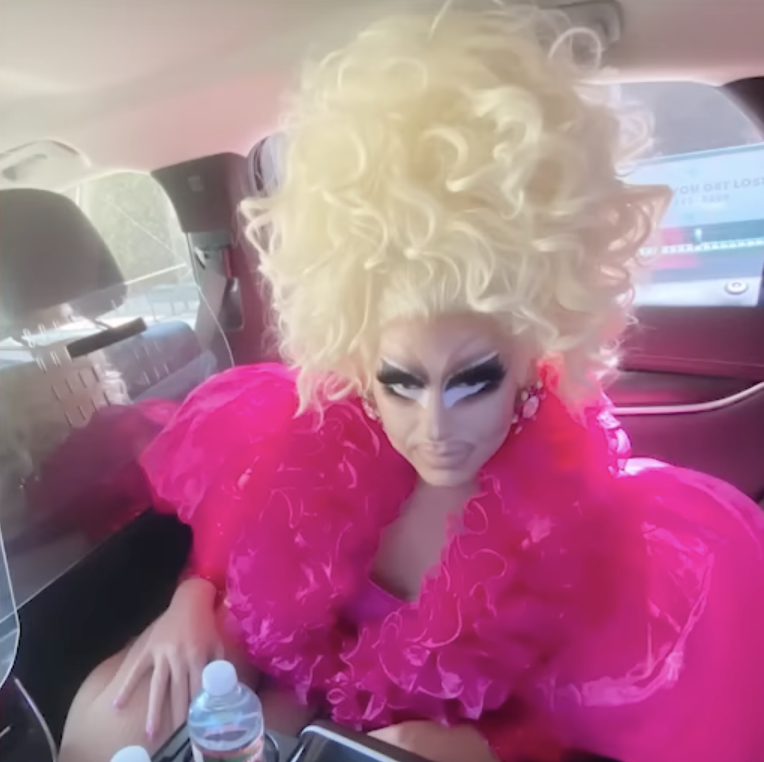 Trixie Mattel in drag, crouching on the floor of a car.